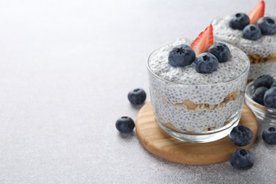 Photo of Superfood. Delicious pudding with chia seeds, yogurt, blueberries, granola and strawberry on light grey table, closeup. Space for text