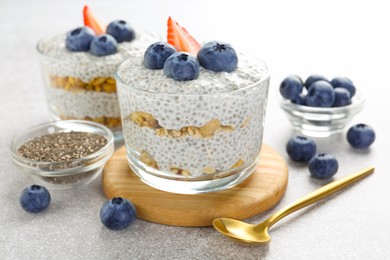 Photo of Delicious pudding with chia seeds, yogurt, blueberries, granola and strawberry on light grey table, closeup. Superfood