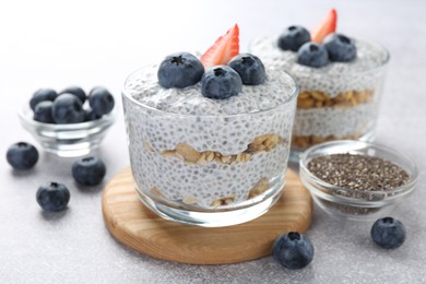 Photo of Delicious pudding with chia seeds, yogurt, blueberries, granola and strawberry on light grey table, closeup. Superfood