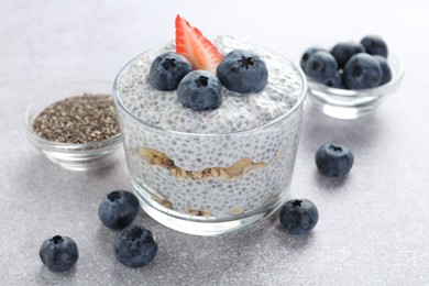 Photo of Delicious pudding with chia seeds, yogurt, blueberries, granola and strawberry on light grey table, closeup. Superfood