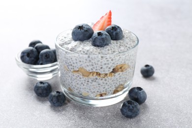 Photo of Delicious pudding with chia seeds, yogurt, blueberries, granola and strawberry on light grey table, closeup. Superfood