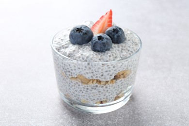 Photo of Delicious pudding with chia seeds, yogurt, blueberries, granola and strawberry on light grey table, closeup. Superfood