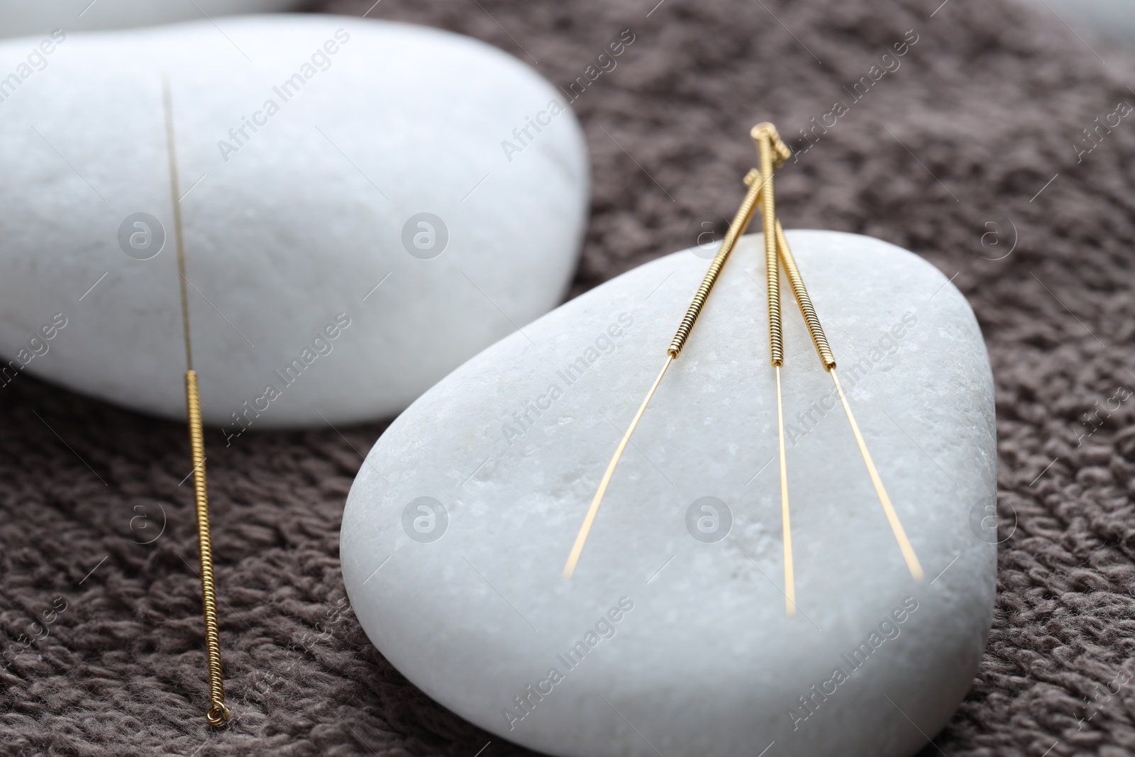 Acupuncture needles and spa stones on brown towel, closeup Photo of Acupuncture needles and spa stones on brown towel, closeup