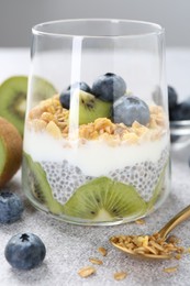 Photo of Delicious dessert with chia seeds, yogurt, granola, blueberries and kiwi on light grey table, closeup. Superfood