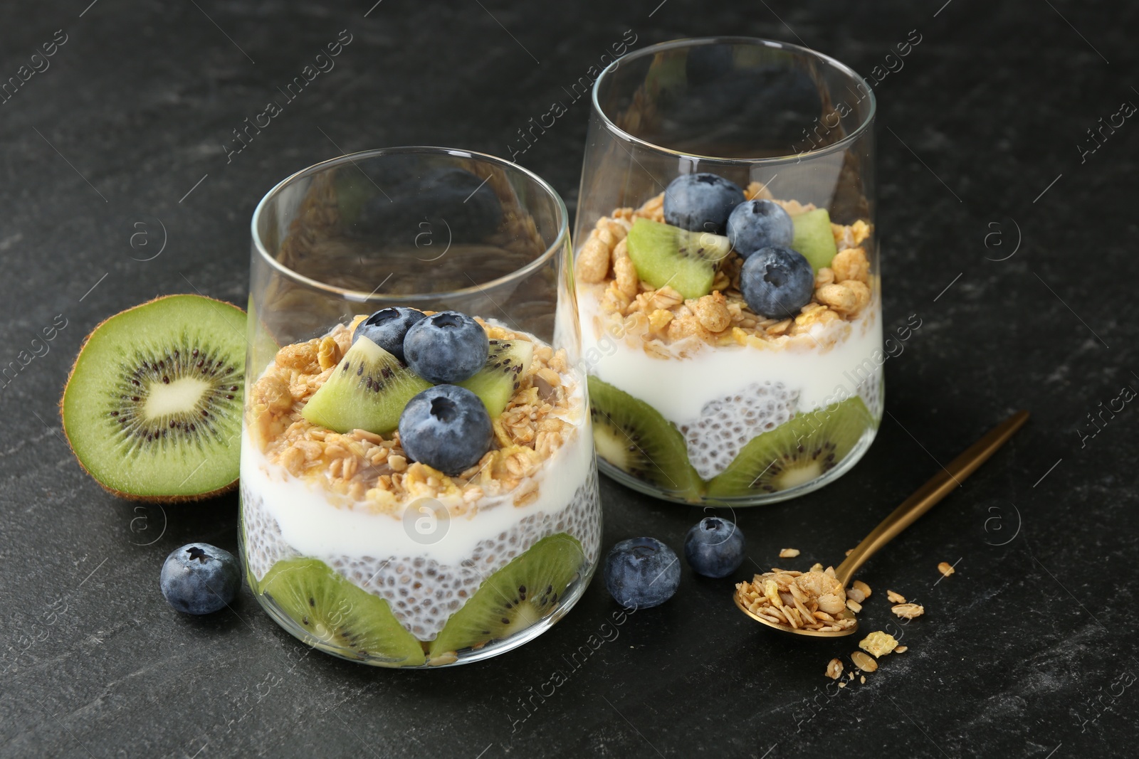 Delicious dessert with chia seeds, yogurt, granola, blueberries and kiwi in glasses on black table, closeup. Superfood Photo of Delicious dessert with chia seeds, yogurt, granola, blueberries and kiwi in glasses on black table, closeup. Superfood