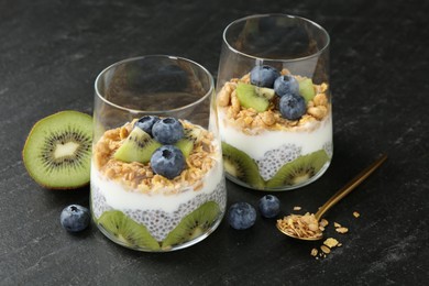 Photo of Delicious dessert with chia seeds, yogurt, granola, blueberries and kiwi in glasses on black table, closeup. Superfood