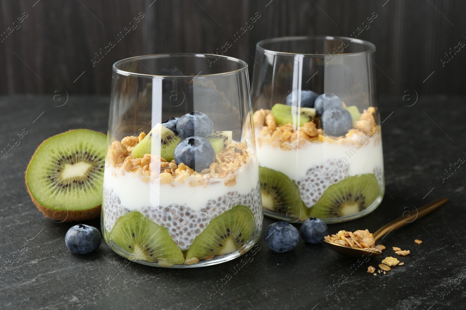 Delicious dessert with chia seeds, yogurt, granola, blueberries and kiwi in glasses on black table, closeup. Superfood Photo of Delicious dessert with chia seeds, yogurt, granola, blueberries and kiwi in glasses on black table, closeup. Superfood