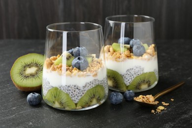 Photo of Delicious dessert with chia seeds, yogurt, granola, blueberries and kiwi in glasses on black table, closeup. Superfood
