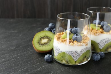 Photo of Superfood. Delicious dessert with chia seeds, yogurt, granola, blueberries and kiwi in glasses on black table, closeup. Space for text