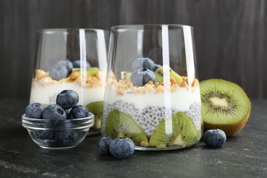 Photo of Delicious dessert with chia seeds, yogurt, granola, blueberries and kiwi in glasses on black table, closeup. Superfood
