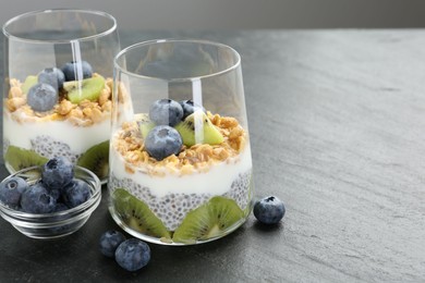 Photo of Superfood. Delicious dessert with chia seeds, yogurt, granola, blueberries and kiwi in glasses on grey table, closeup. Space for text