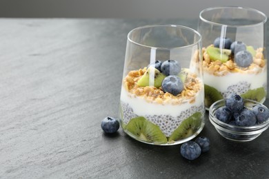 Photo of Superfood. Delicious dessert with chia seeds, yogurt, granola, blueberries and kiwi in glasses on grey table, closeup. Space for text