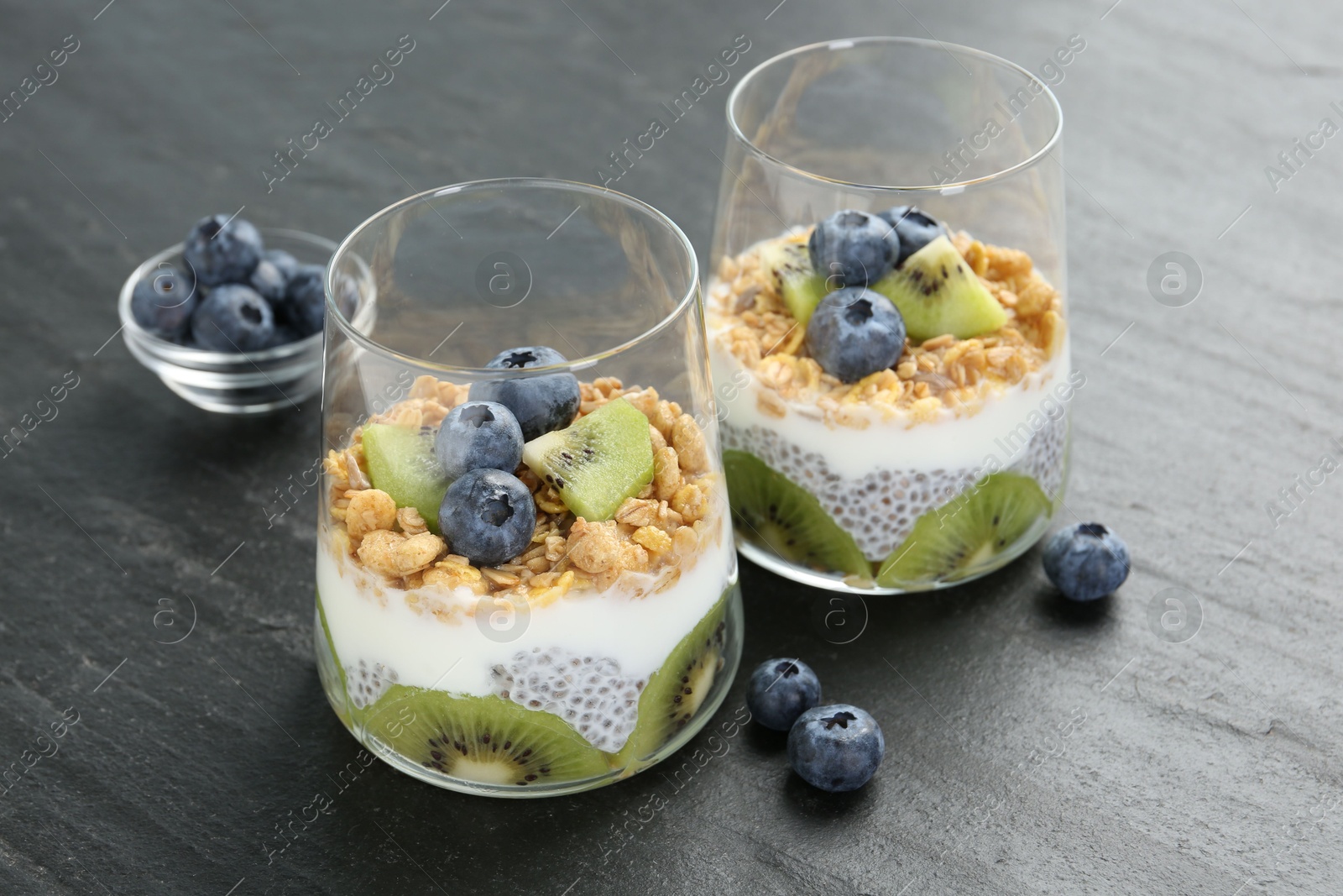 Delicious dessert with chia seeds, yogurt, granola, blueberries and kiwi in glasses on grey table, closeup. Superfood Photo of Delicious dessert with chia seeds, yogurt, granola, blueberries and kiwi in glasses on grey table, closeup. Superfood
