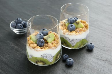 Photo of Delicious dessert with chia seeds, yogurt, granola, blueberries and kiwi in glasses on grey table, closeup. Superfood