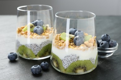 Photo of Delicious dessert with chia seeds, yogurt, granola, blueberries and kiwi in glasses on grey table, closeup. Superfood