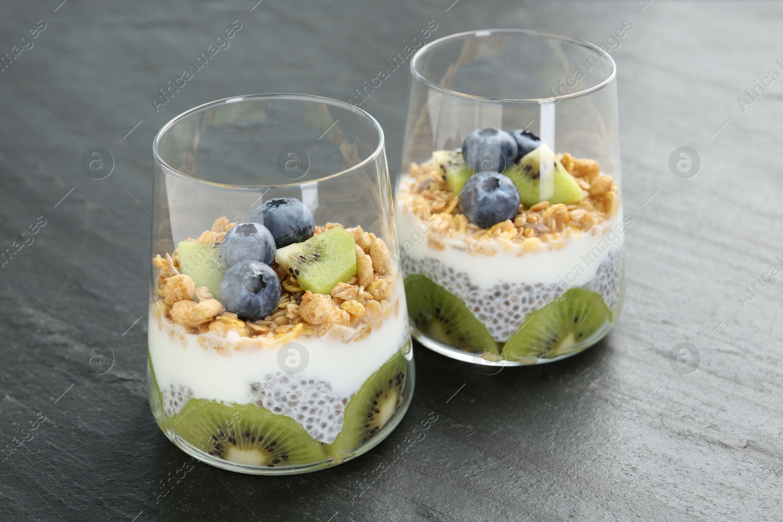 Delicious dessert with chia seeds, yogurt, granola, blueberries and kiwi in glasses on grey table, closeup. Superfood Photo of Delicious dessert with chia seeds, yogurt, granola, blueberries and kiwi in glasses on grey table, closeup. Superfood