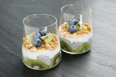 Photo of Delicious dessert with chia seeds, yogurt, granola, blueberries and kiwi in glasses on grey table, closeup. Superfood