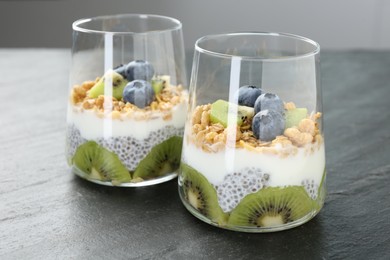 Photo of Delicious dessert with chia seeds, yogurt, granola, blueberries and kiwi in glasses on grey table, closeup. Superfood