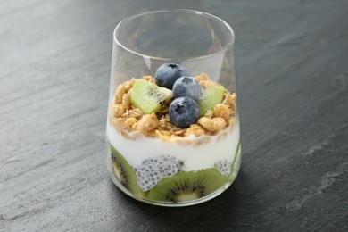 Photo of Delicious dessert with chia seeds, yogurt, granola, blueberries and kiwi in glass on grey table, closeup. Superfood