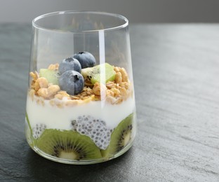 Photo of Superfood. Delicious dessert with chia seeds, yogurt, granola, blueberries and kiwi in glass on grey table, closeup. Space for text