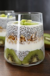 Photo of Delicious dessert with chia seeds, yogurt, granola and kiwi on wooden table, closeup. Superfood