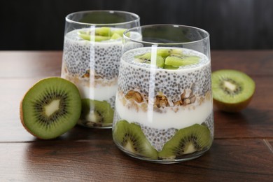 Photo of Delicious dessert with chia seeds, yogurt, granola and kiwi on wooden table, closeup. Superfood