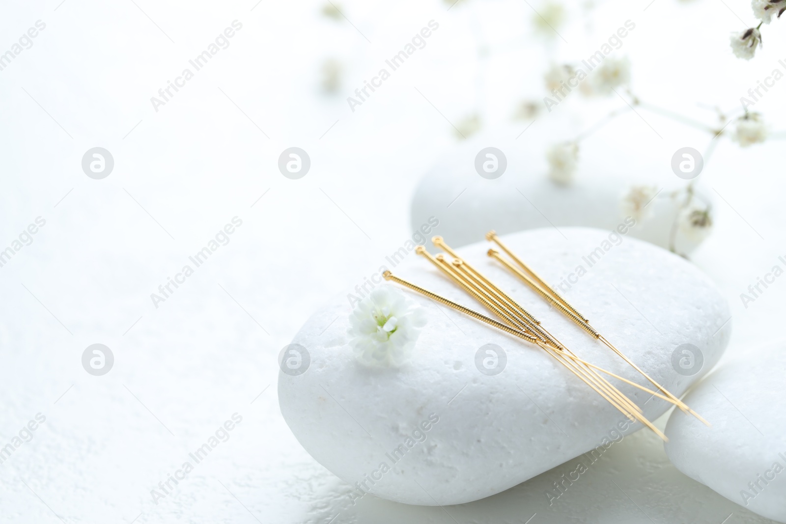 Acupuncture needles, pebble stones and flower bud on white textured table, closeup. Space for text Photo of Acupuncture needles, pebble stones and flower bud on white textured table, closeup. Space for text