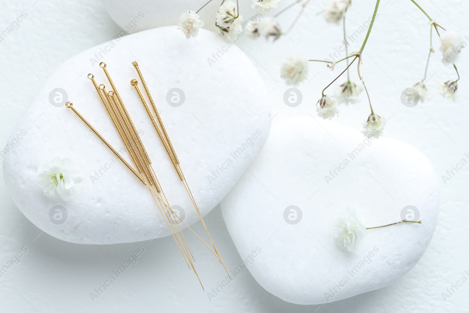 Acupuncture needles, pebble stones and flowers on white table, flat lay Photo of Acupuncture needles, pebble stones and flowers on white table, flat lay
