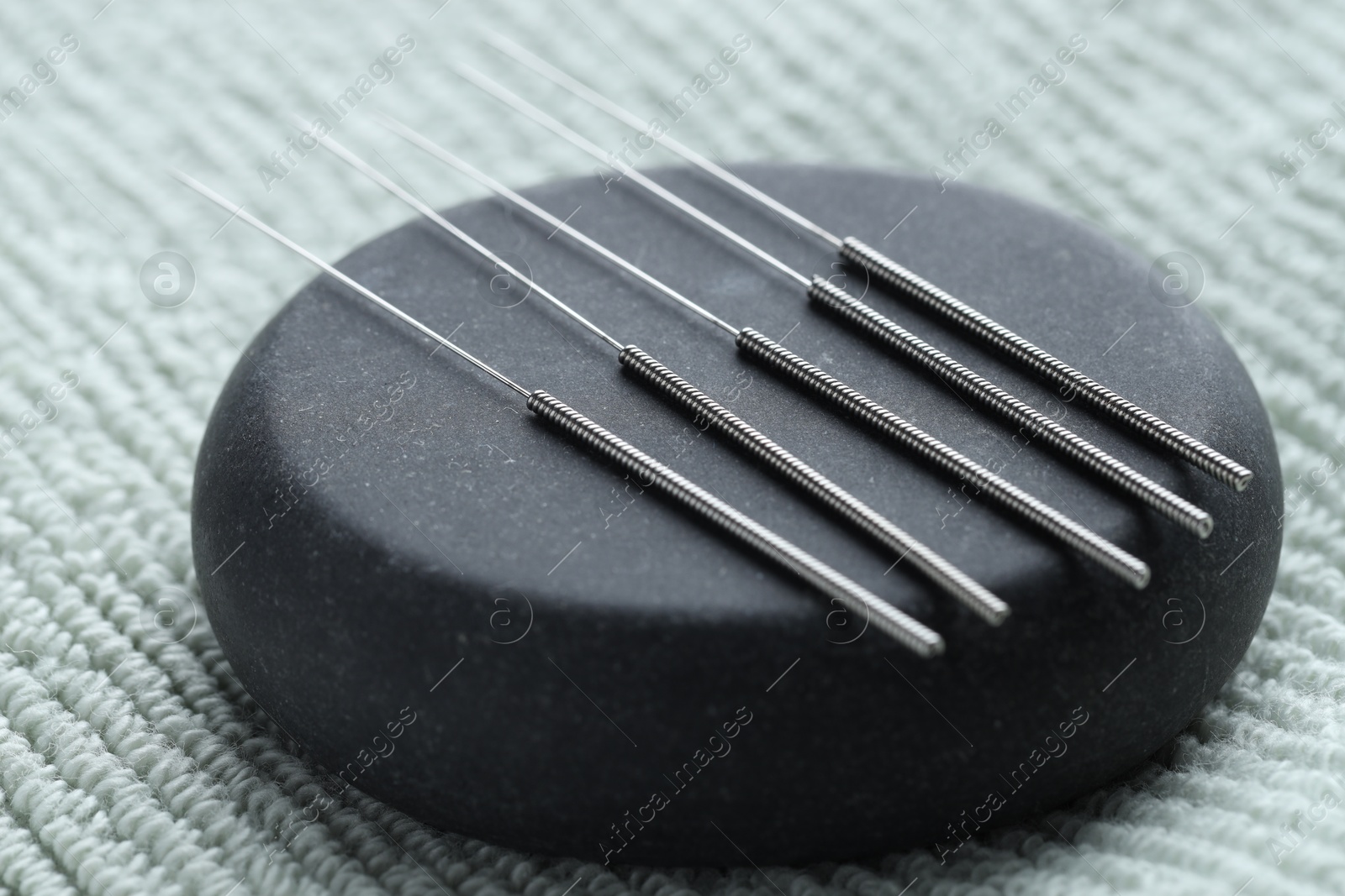Acupuncture needles and pebble stone on green towel, closeup Photo of Acupuncture needles and pebble stone on green towel, closeup