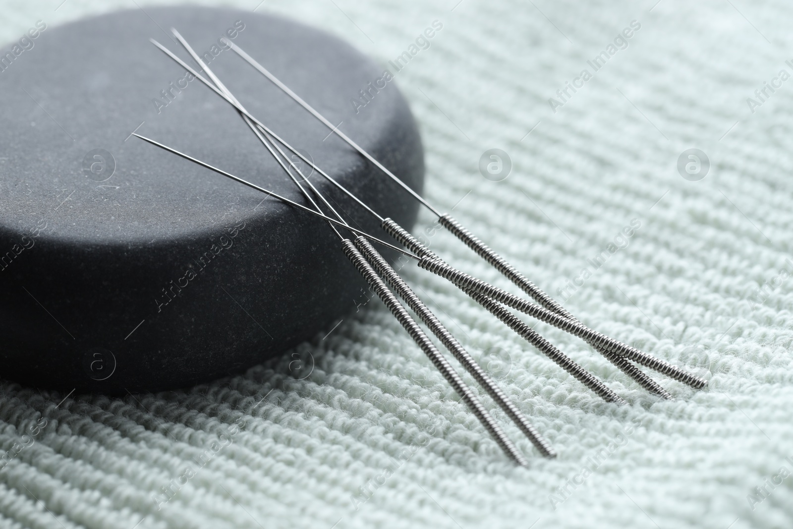 Acupuncture needles and pebble stone on green towel, closeup Photo of Acupuncture needles and pebble stone on green towel, closeup