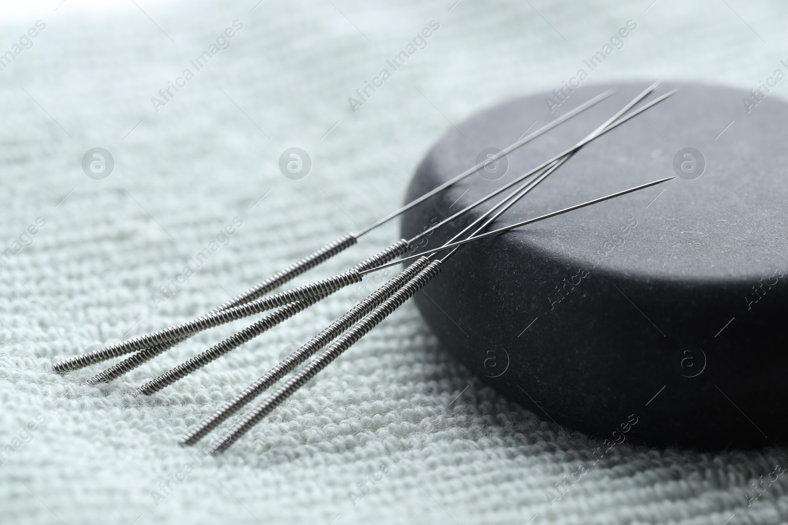 Acupuncture needles and pebble stone on green towel, closeup Photo of Acupuncture needles and pebble stone on green towel, closeup