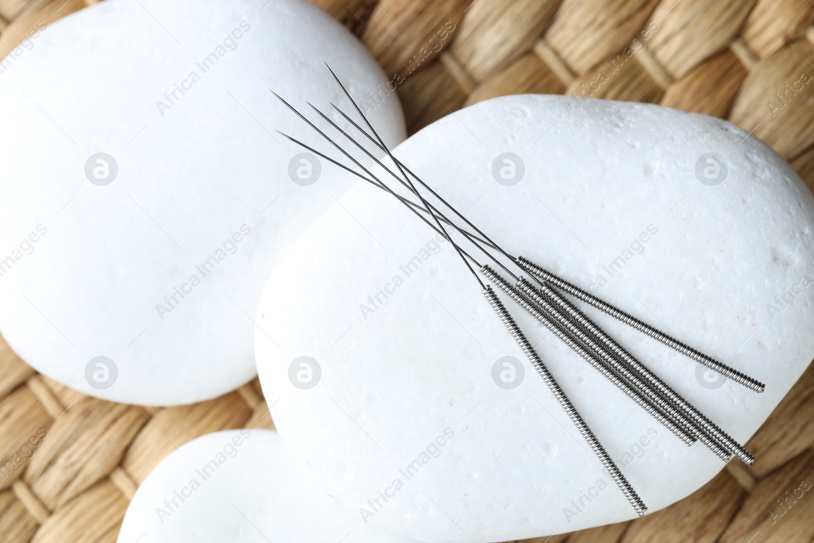 Acupuncture needles and pebble stones on wicker surface, above view Photo of Acupuncture needles and pebble stones on wicker surface, above view