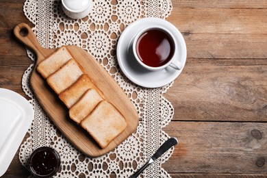 Photo of Slices of tasty toasted bread, jam and cup of tea on wooden table, flat lay. Space for text