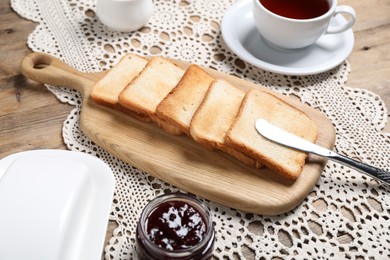 Photo of Slices of tasty toasted bread, jam and cup of tea on wooden table, closeup