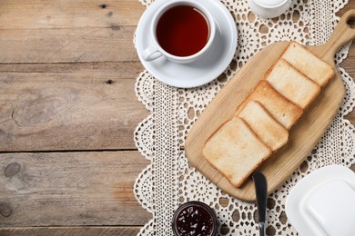 Photo of Slices of tasty toasted bread, jam and cup of tea on wooden table, flat lay. Space for text