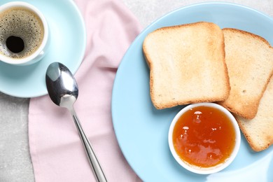 Photo of Slices of tasty toasted bread, jam and cup of coffee on grey table, flat lay