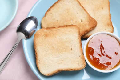 Photo of Slices of tasty toasted bread, jam and spoon on pink tablecloth, top view