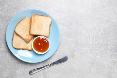 Photo of Slices of tasty toasted bread, jam and knife on grey textured table, flat lay. Space for text