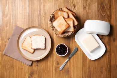Photo of Slices of tasty toasted bread, butter and jam on wooden table, flat lay