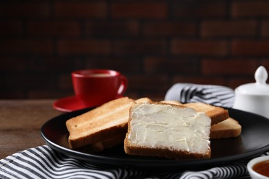 Photo of Slices of tasty toasted bread with butter on wooden table against dark background, closeup