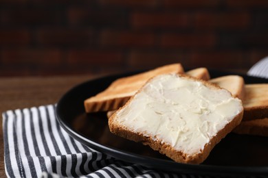 Photo of Slices of tasty toasted bread with butter on table against dark background, closeup
