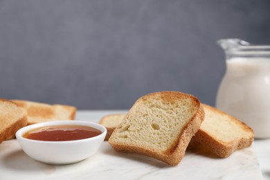 Photo of Slices of tasty toasted bread, milk and jam on white table against grey background, closeup