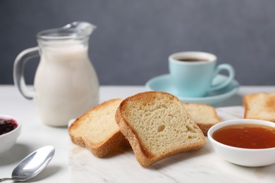 Photo of Slices of tasty toasted bread, milk and jam on white table against grey background, closeup