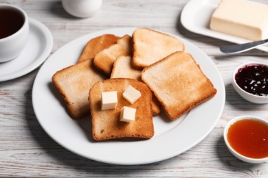 Photo of Slices of tasty toasted bread with butter and jam on light wooden table, closeup