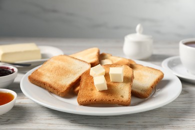 Photo of Slices of tasty toasted bread with butter on light wooden table against grey background, closeup