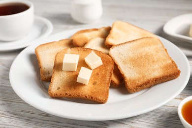 Photo of Slices of tasty toasted bread with butter on light wooden table, closeup