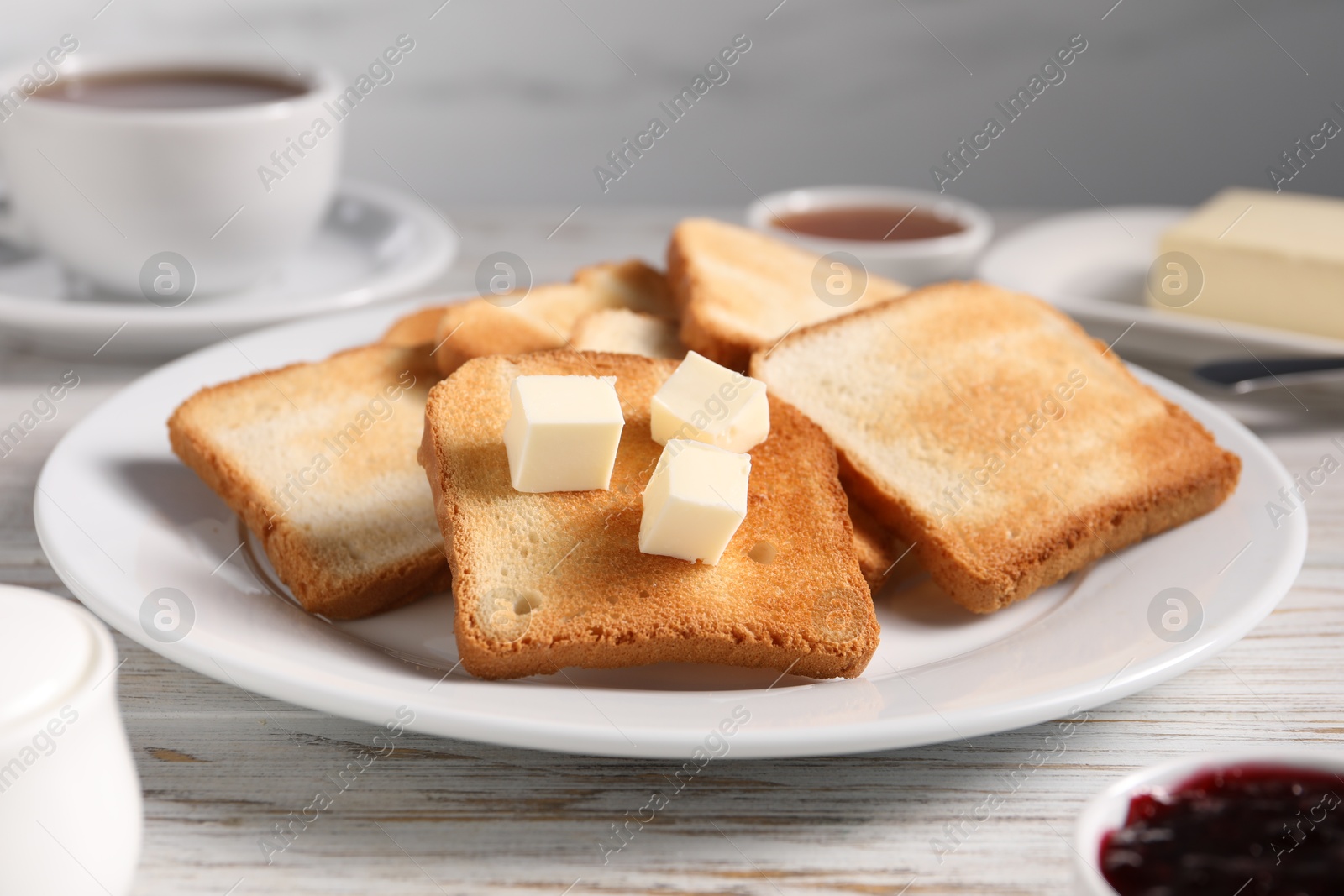 Slices of tasty toasted bread with butter on light wooden table against grey background, closeup Photo of Slices of tasty toasted bread with butter on light wooden table against grey background, closeup