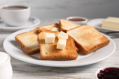 Photo of Slices of tasty toasted bread with butter on light wooden table against grey background, closeup