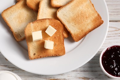 Photo of Slices of tasty toasted bread with butter and jam on light wooden table, flat lay