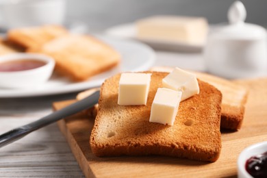Photo of Slices of tasty toasted bread with butter on light wooden table against grey background, closeup